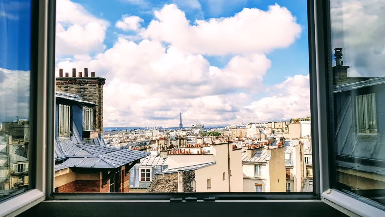 Vue de Paris depuis une fenêtre, avec la tour Eiffel au loin.