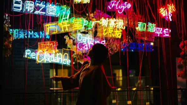 Photo of a woman standing amid dozens of neon signs in various languages.
